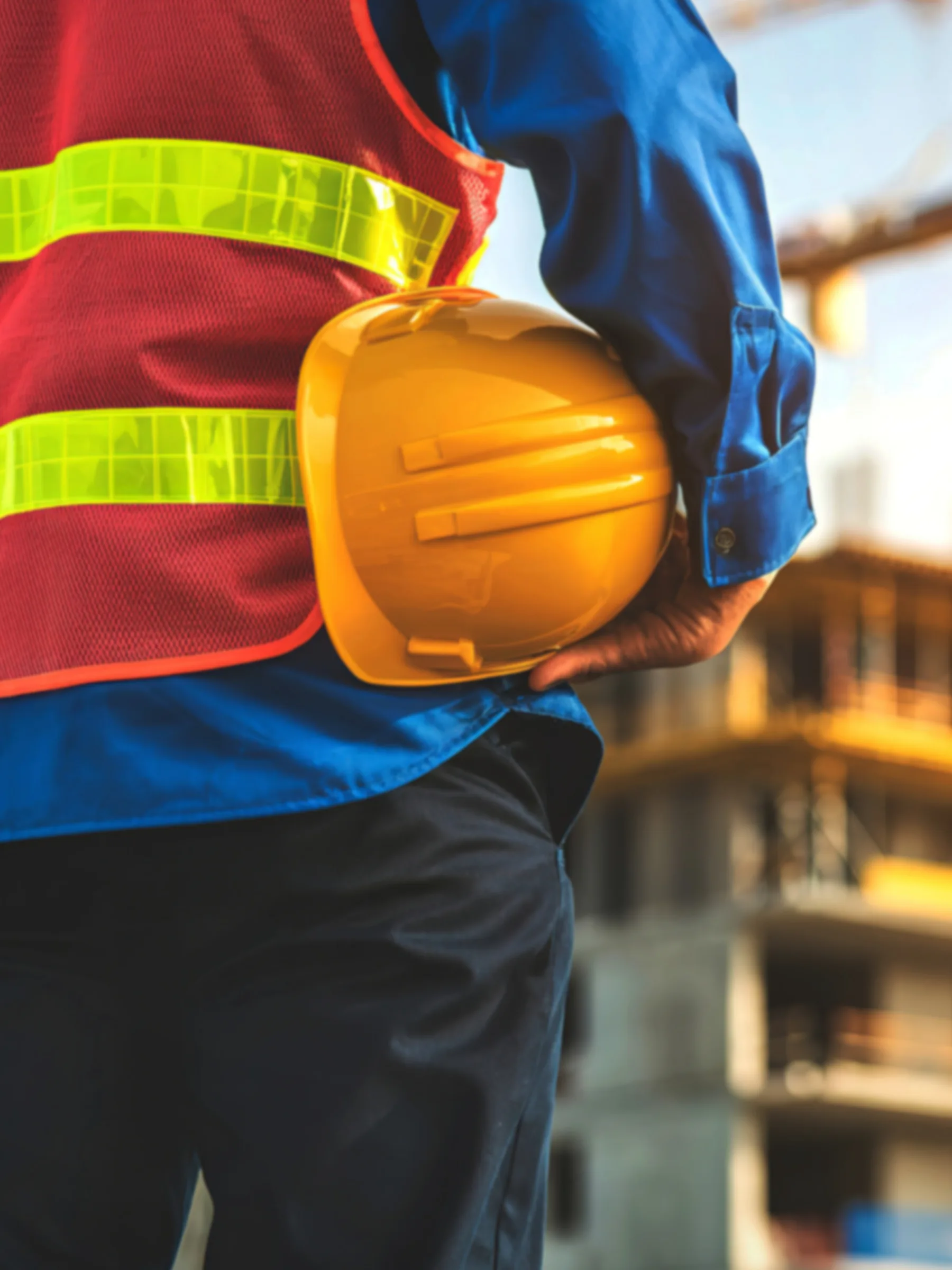 Construction worker in a hi-vis vest holding a yellow hard hat at a building site — construction jobs in Malta